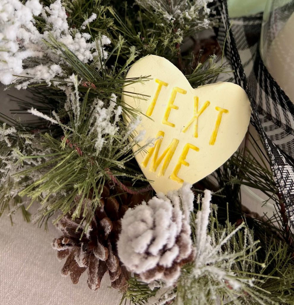 Closeup of a large clay conversation heart that says Text ME nestled in greenery of a centerpiece
