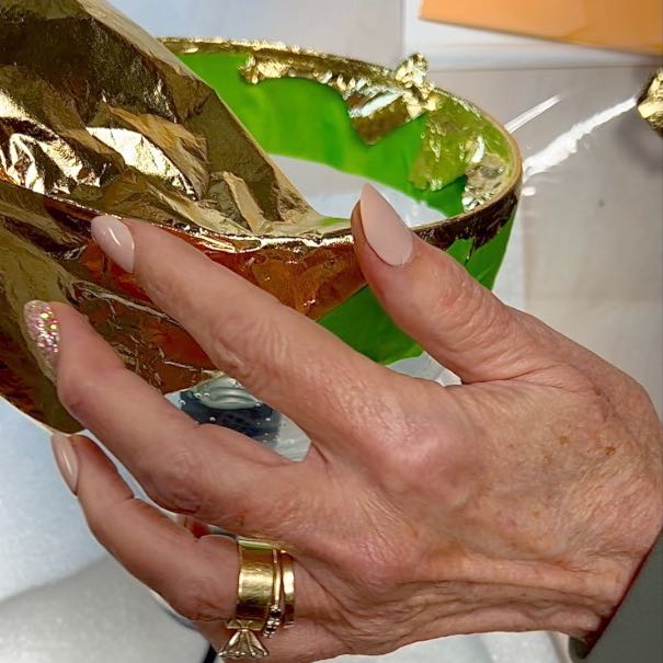 closeup of woman's hands applying sheet of gold leaf to the edge of the glass shade