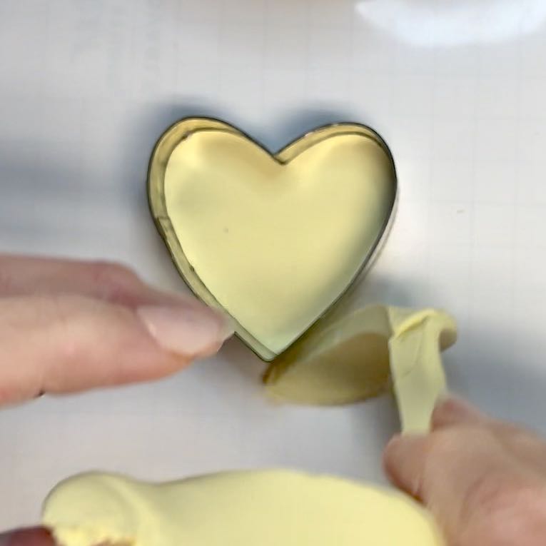 woman'r fingers are pulling the excess clay away from the heart-shaped cookie cutter