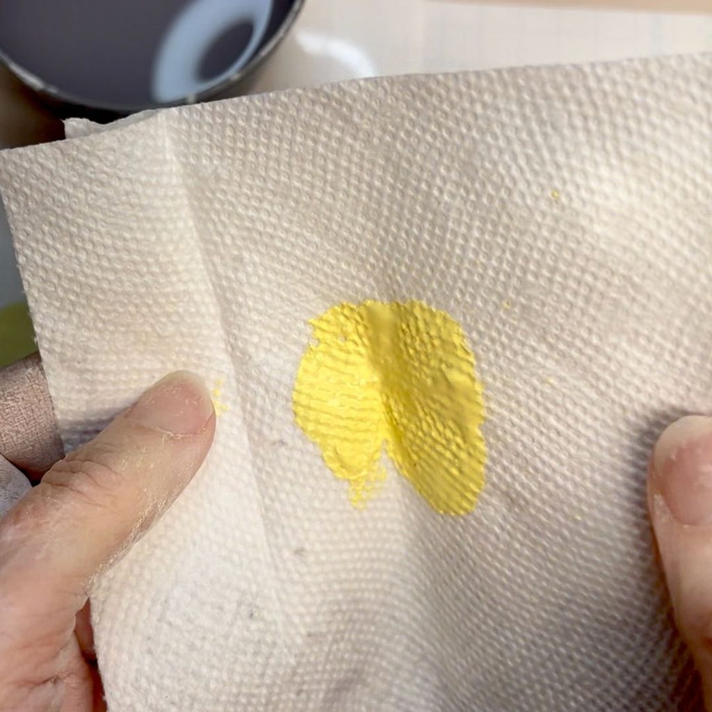 woman's fingers are holding a paper towel folded with yellow paint in the center