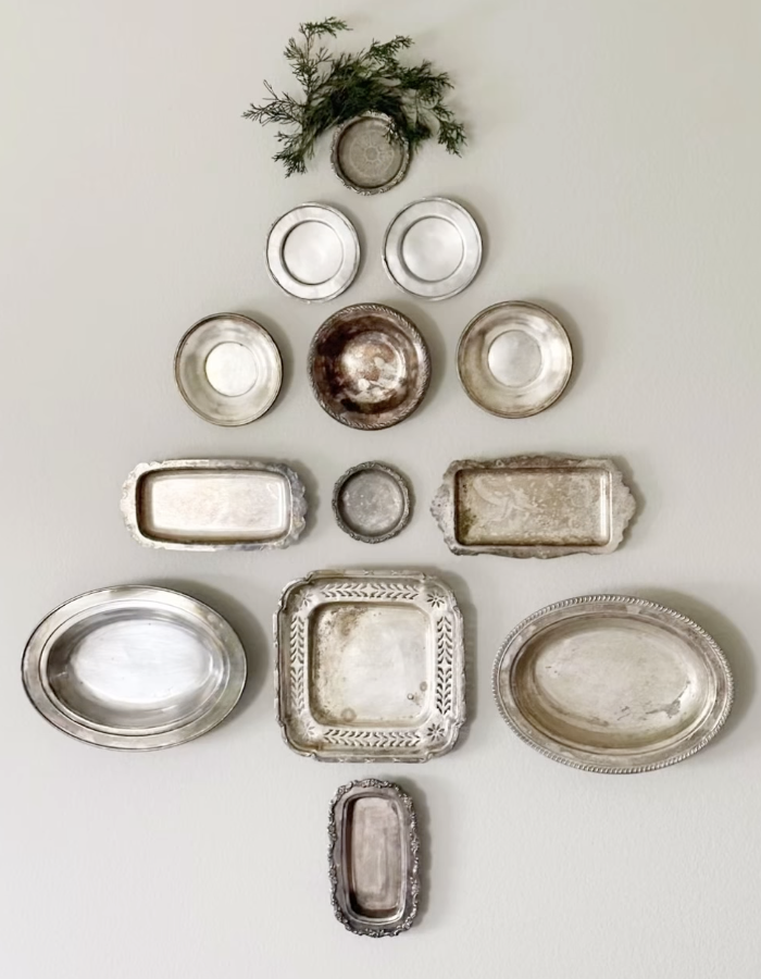 Vintage silver dishes and trays arranged on a wall in the shape of a Christmas tree