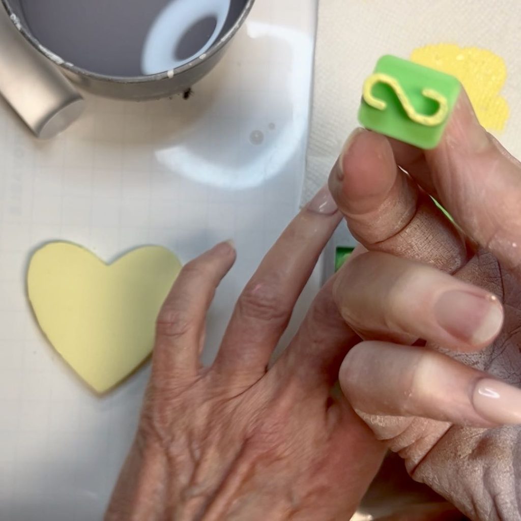 woman's hand holing an "S" stamp dipped ini yellow paint