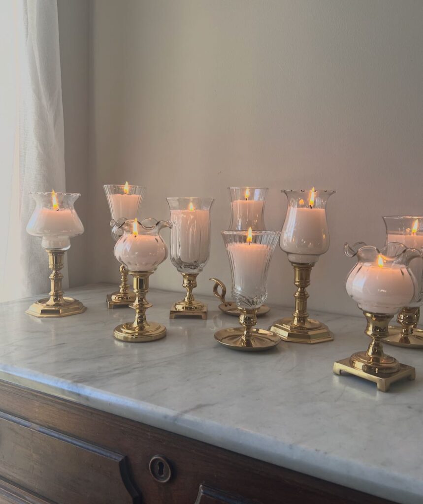 mismatched filled hurricane candle are lit on a marble topped chest