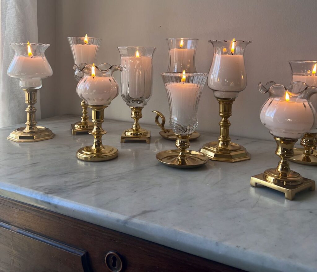 mismatched filled hurricane candle are lit on a marble topped chest