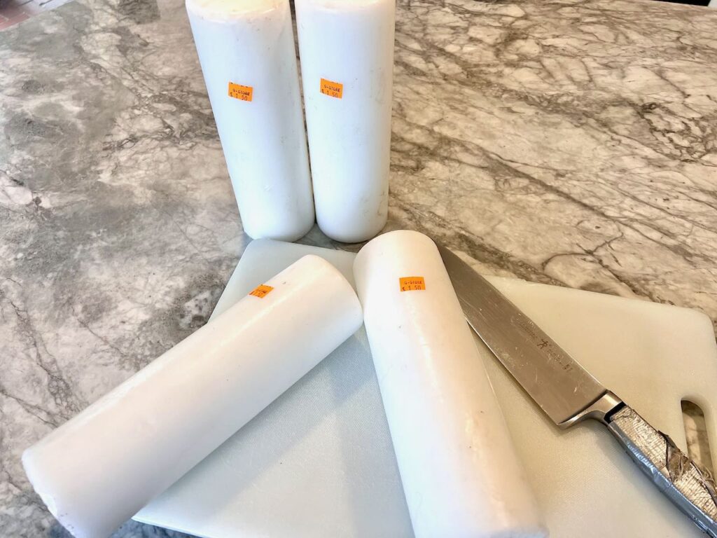 Four large pillar candles resting on a cutting board with a chef's knife nearby