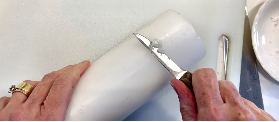 closeup of knife scraping dirt spots off a pillar candle