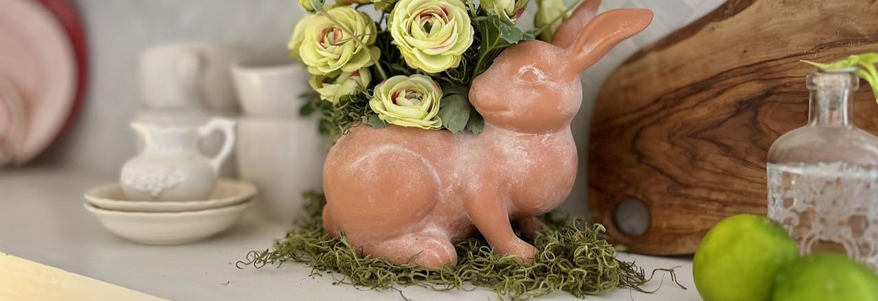 wide closeup of aged Terracotta bunny planter filled with Ranunculus flowers is sitting on a kitchen shelf