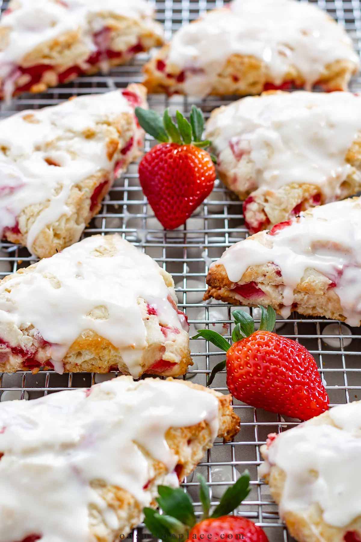 strawberry scones are on a cooling rack with fresh strawberries and glaze poured over them