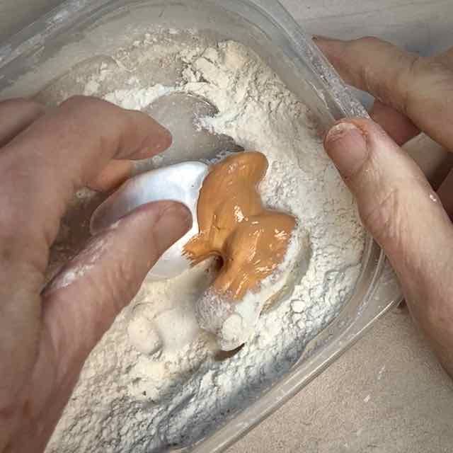 the front half of the bunny with wet paint is being dipped in the container of flour