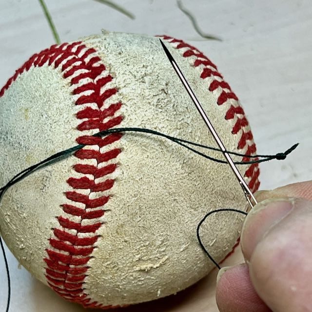 needle drawing thread back through the original threads around baseball lacing