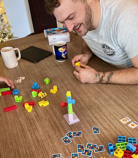 man smiling while looking intently at a tower of wobbling game pieces