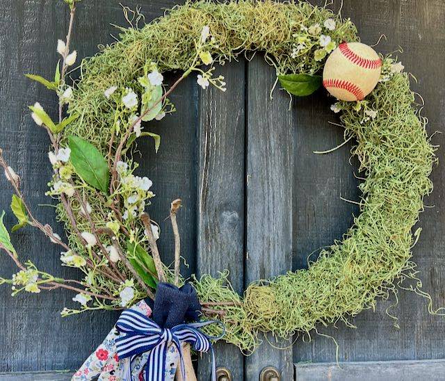 view of a moss wreath decorating fro Spring with garden gloves and tool and an od baseball