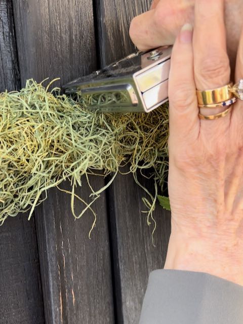 woman's hands are using staple gun to attach the top of the wreath to the door