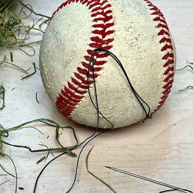 closeup of baseball with a thread from a needle is under the placing of the baseball
