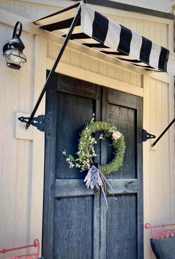 a Split wreath is hanging across a pair of double doors under a stripe awning
