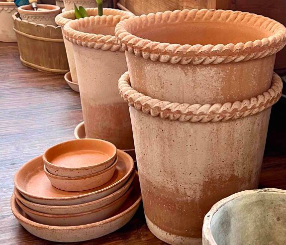 Stacks of large terra cotta pots are on a wood floor
