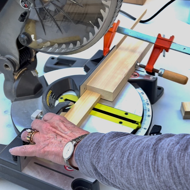 closeup of woman using a miter saw set with a wood block jig to cut identical length wood blocks