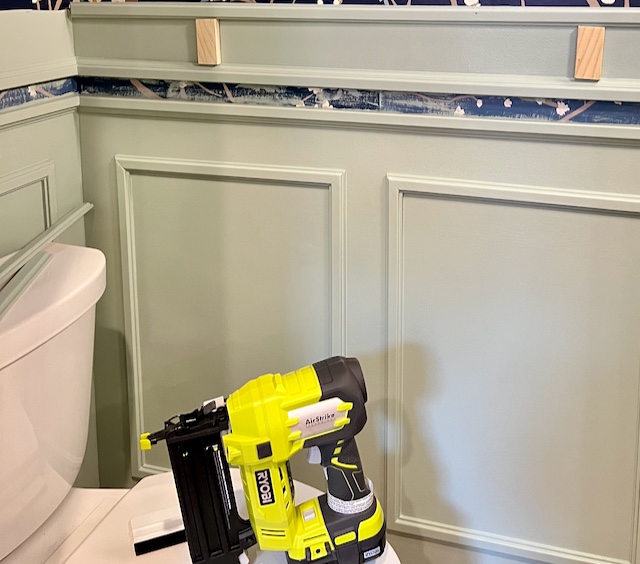 spacer blocks are shown between the chair rail and the top trim with a nail gun ready to go