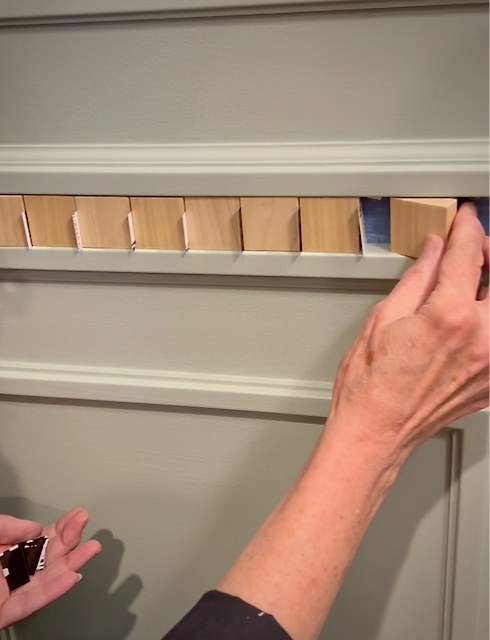 woman's hands holding spacers and adding a wood block to the chair rail