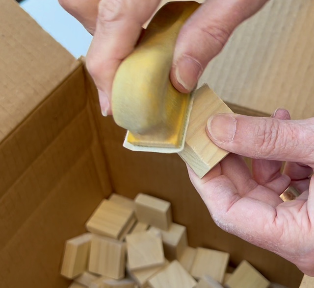 closeup of woman's fingertips holding a detailll sander against small wood blocks