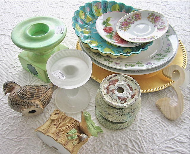 a pile of odd shaped dishes, candlesticks and statues in on a table. Some with thrift store price tags attached