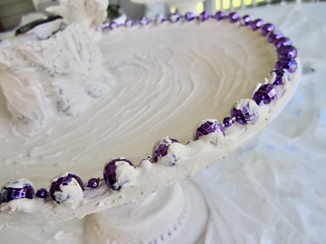 closeup of large mardi gras beads stuck in a bed of joint compound around the lip of a plate to become the water basin