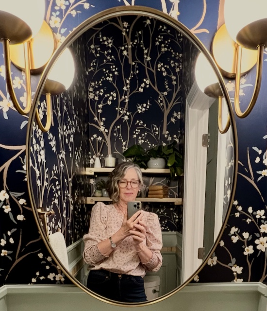 woman shooting picture on iPhone is reflected in a closeup of the mirror hung close between two lit wall sconces