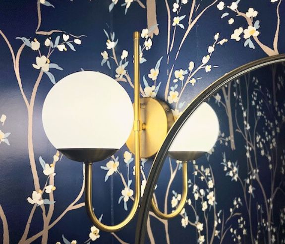 closeup side view of one lit light fixture with top part of mirror beside it