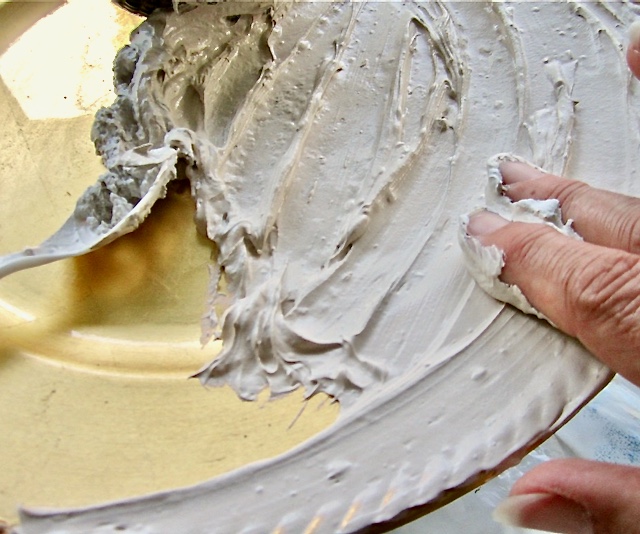 closeup of fingertips spreading the first layer of joint compound on a large plate