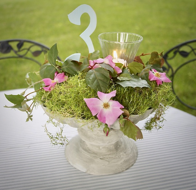 finished birdbath centerpieces is shown with live moss and wild rose blooms with a lit candle in a hurricane and a table number