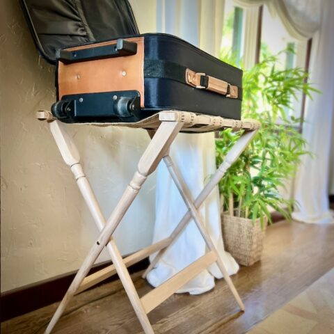 a medium suitcase is open on a upcycled luggage rack by a window with long linen curtains