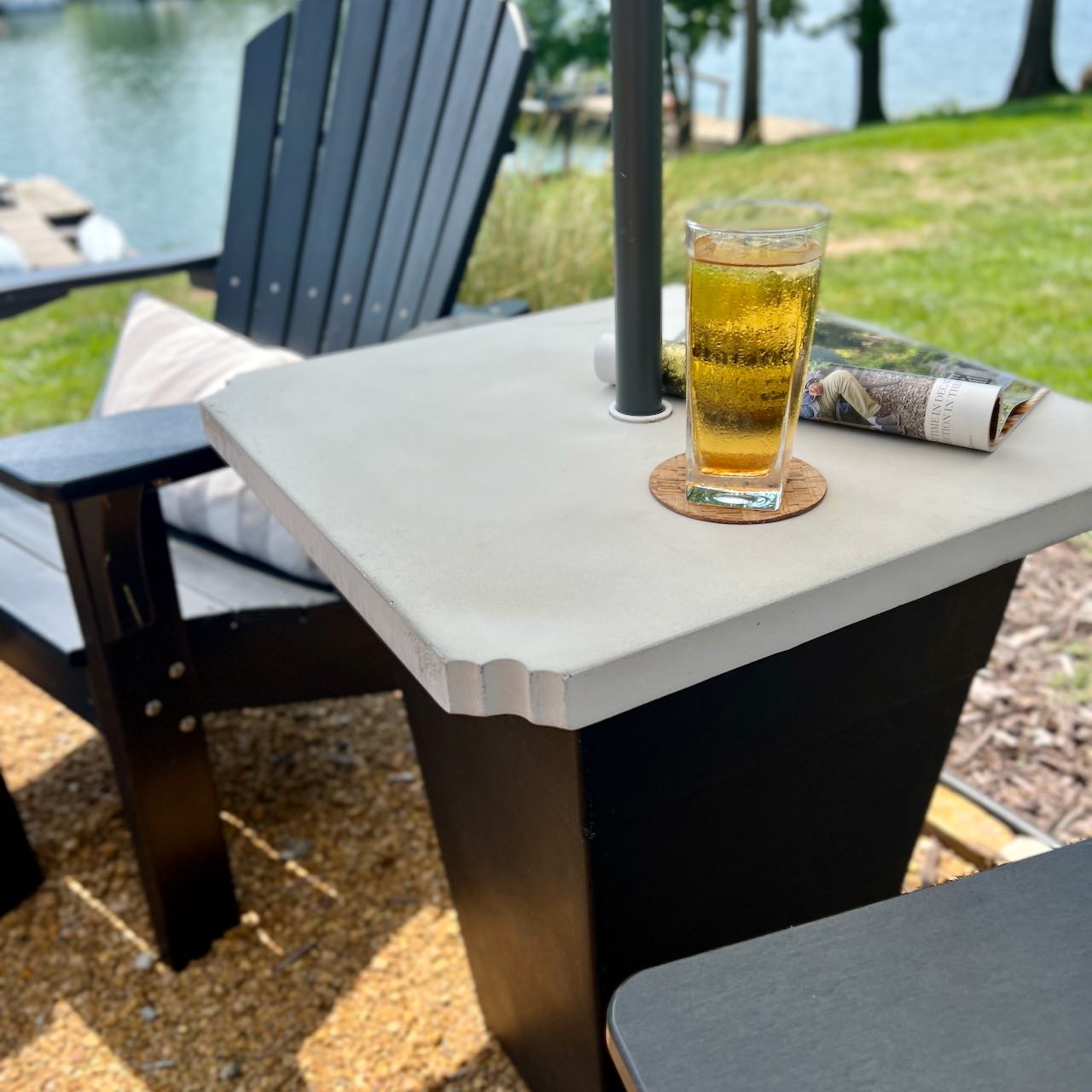 view of thee finished umbrella side table with concrete top with lawn and lake in background