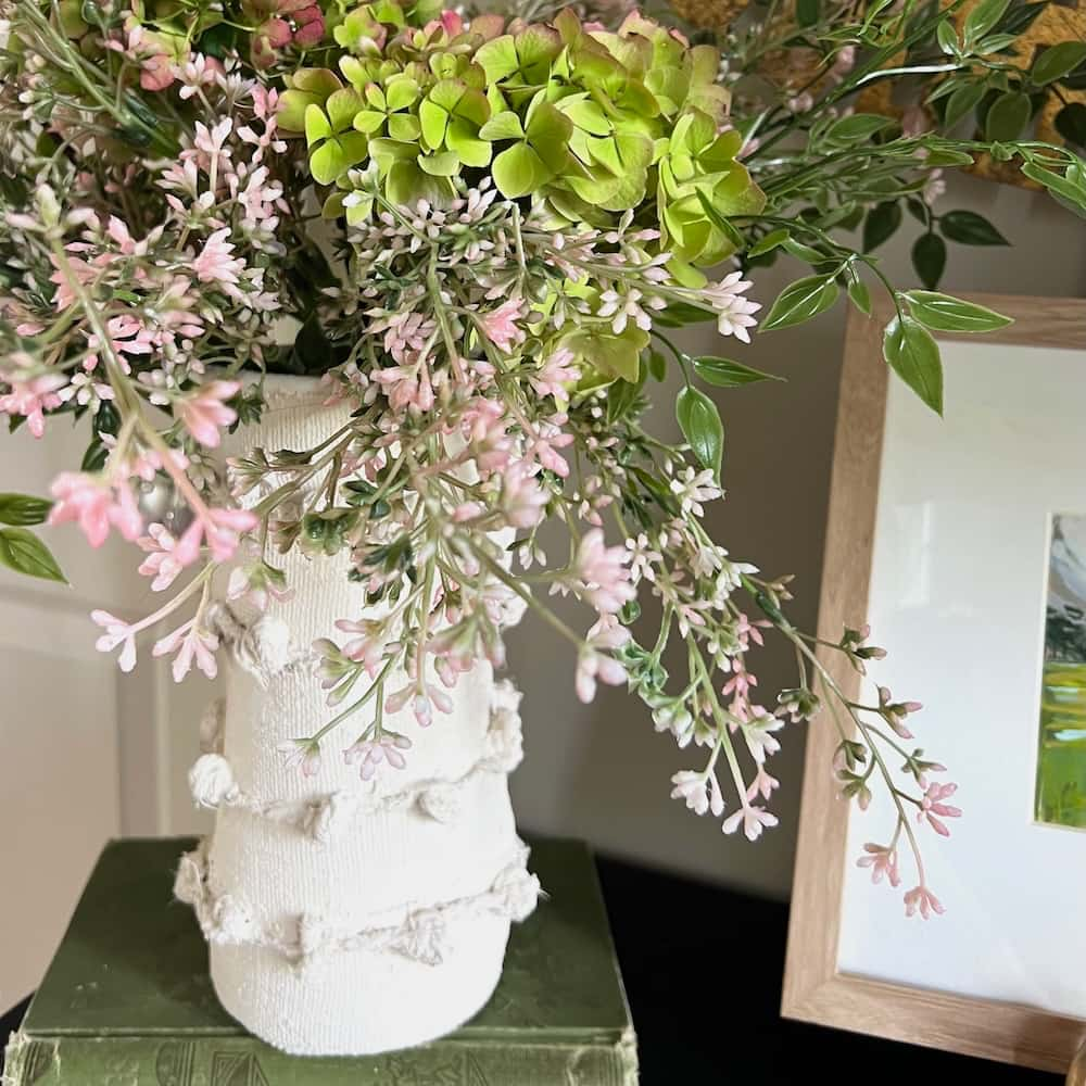 a tall vase made of jute twine filled with a casual flower arrangement spilling out of the top