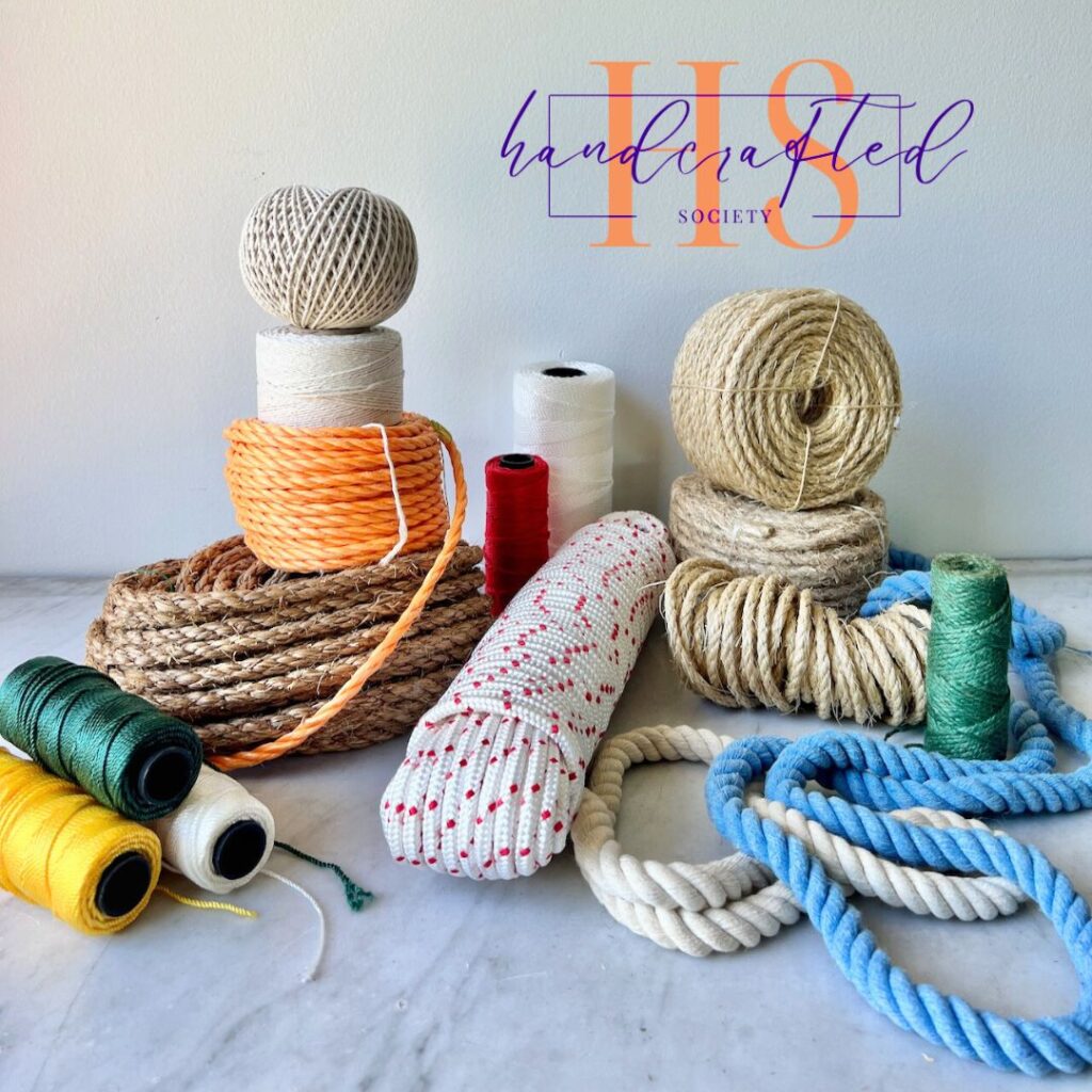 an assortment of ropes and twine are gathered in a display of a marble table top under the Handcrafted Society logo