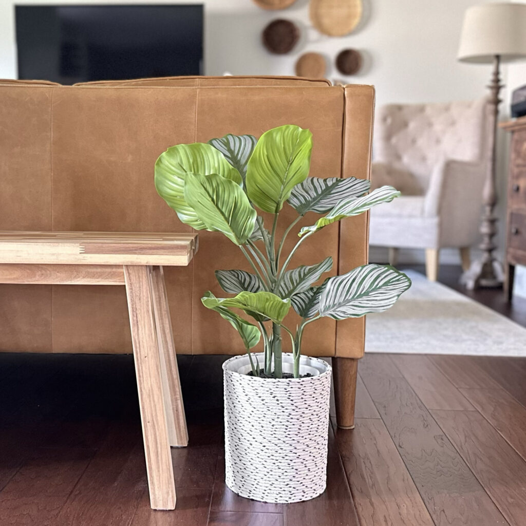 a tall planter basket made of two-toned tope shown behind a leather couch and wood bench