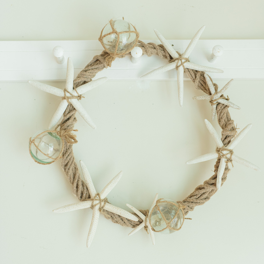 coastal wreath made of jute wrapped wreath and embellished with sand dollars and glass buoys hanging on a peg rack