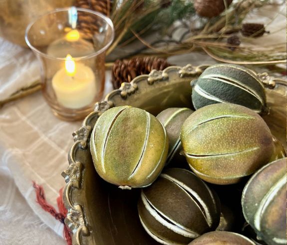 a votive candle in the background partially illuminates a pile of whole dried limes in a vintage silver decorative bowl