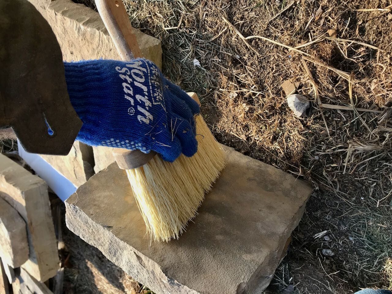 A gloved hand using a stiff brush to clean off a stonebrushing off