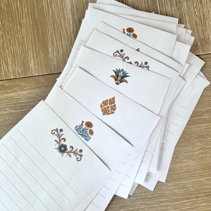 A stack of lined notecards with various decorative floral and botanical designs at the top, laid out on a light wooden surface.