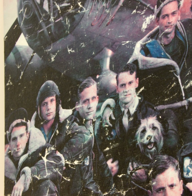 A vintage, scratched photo reminiscent of vintage poster artwork shows five men in military uniforms and flight gear posing before an aircraft, with a dog sitting among them. The image features visible wear and damage.