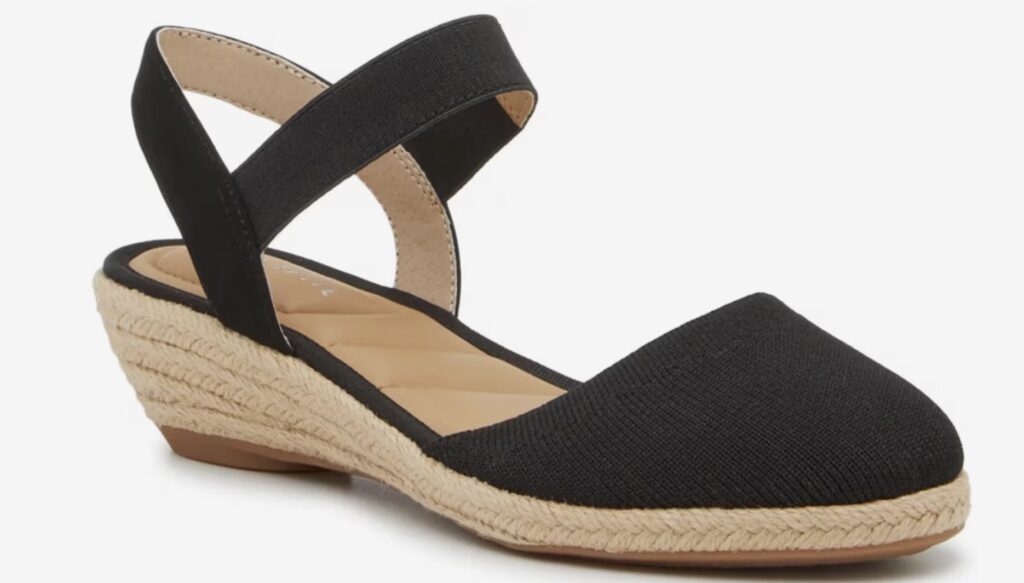 A black espadrille wedge sandal with a closed toe, elastic strap over the instep, tan insole, and woven jute-wrapped sole.