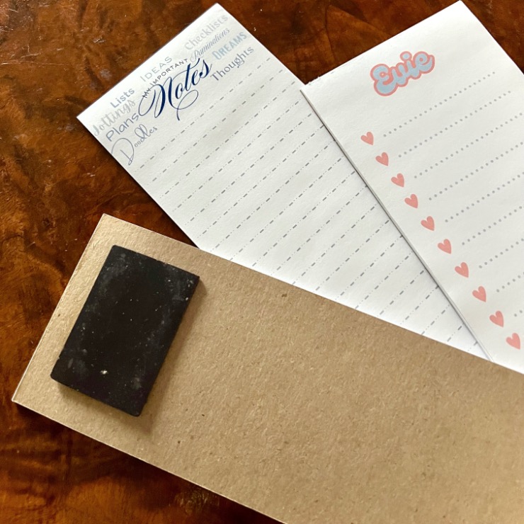Three notepads on a wooden surface: one with light blue headings and "Notes" in script, one with "Errie" and pink hearts, and one plain brown with a black eraser on top.