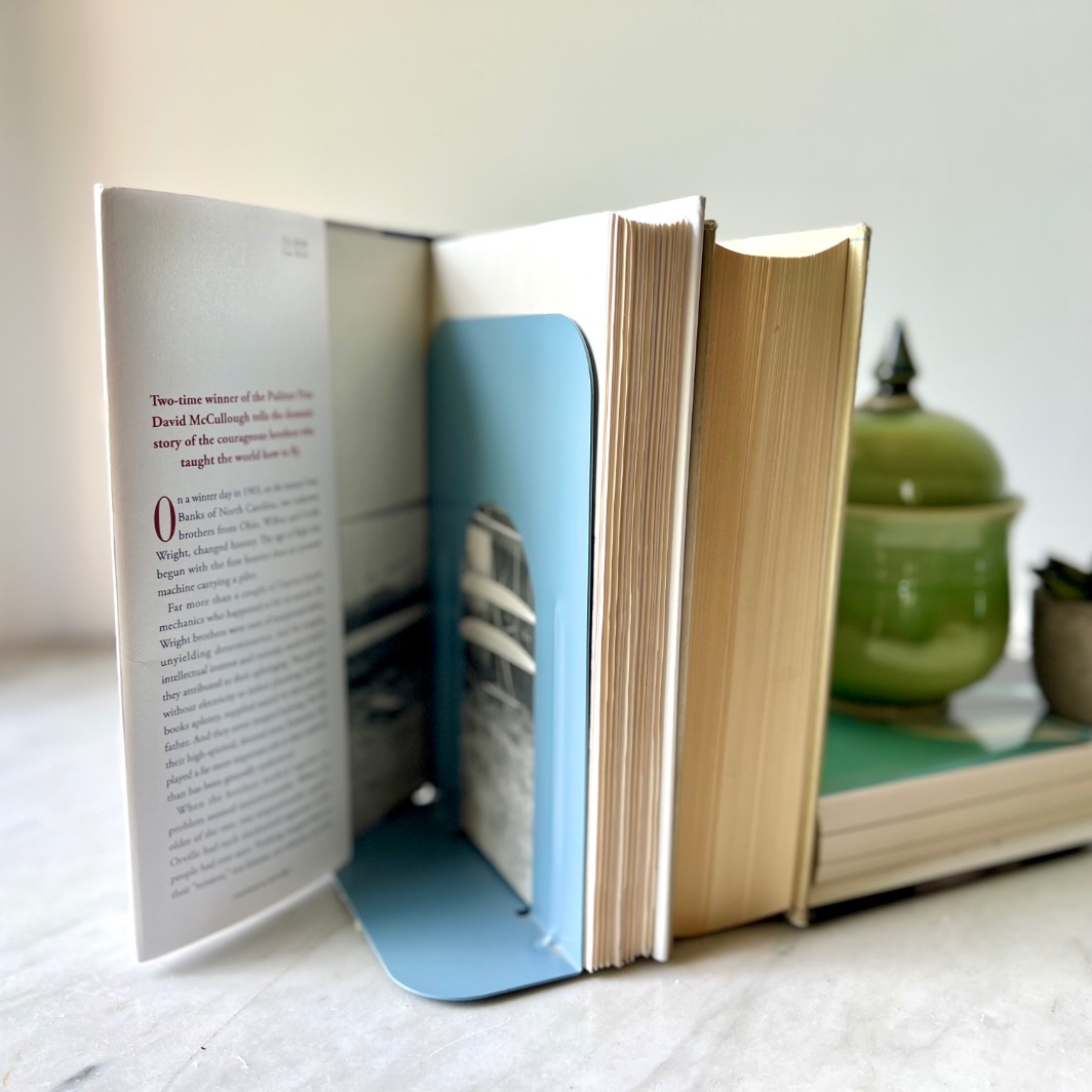 An open book with a blue bookend sits beside a closed book, a green teapot, and a small succulent on a light surface—perfect for styling alongside floating bookshelves.