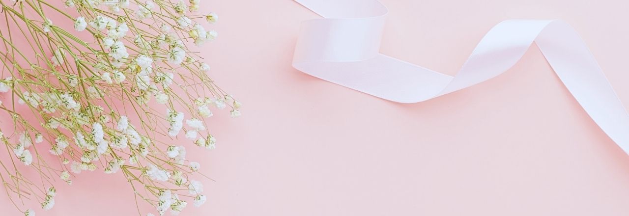 Delicate white baby's breath flowers on the left side and a white satin ribbon curling across a soft pink background—perfect inspiration for blended family wedding gifts.