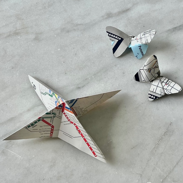 Wondering what to do with old maps? Here, a folded star and two butterflies crafted from a subway map are displayed on a light gray marble surface.