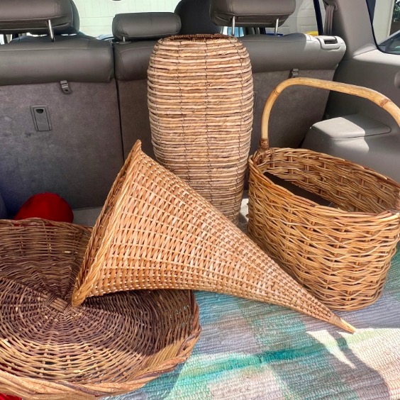 Four woven wicker baskets of different shapes and sizes are arranged in the back of a car, alongside a charming DIY witch hat decor, with the rear seats visible and a mat underneath the baskets.