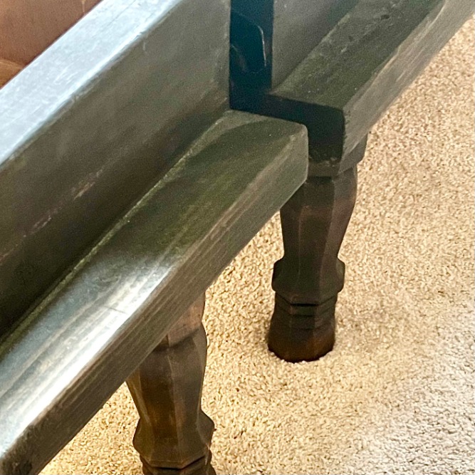 A close-up of two dark wooden benches with angled edges, positioned closely together on a beige carpeted floor—perfectly complementing spaces from twin beds to X-Long. The benches feature sturdy, carved legs and their corners almost touch.