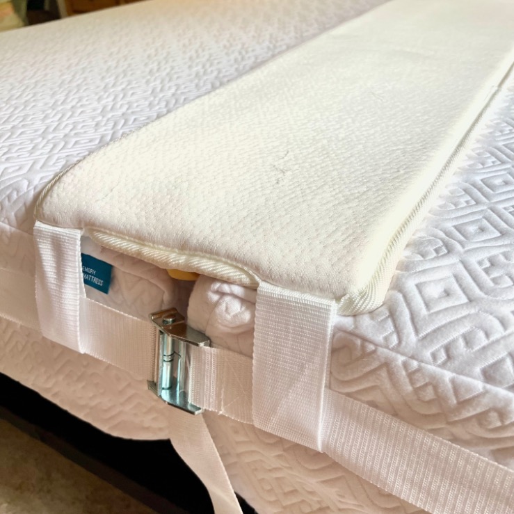A close-up of a mattress gap filler secured between twin beds to X-Long mattresses with a white strap and metal buckle, connecting the beds to create a larger, even sleeping surface.