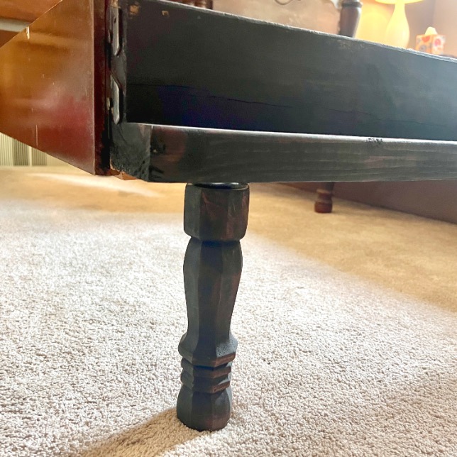 A close-up of a wooden drawer partially open, showing a decorative dark wood leg supporting the drawer bottom, on a light-colored carpeted floor—perfect for bedrooms with twin beds to X-Long.