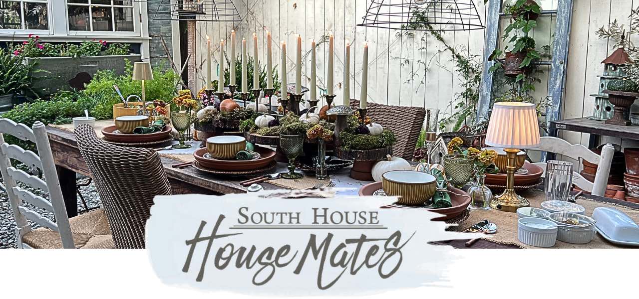 A rustic outdoor dining table is set with candles, plates, and autumn-themed decor. Plants and greenery surround the area. Text overlay reads “South House House Mates.”.